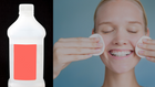 A close-up of a transparent bottle, typically used for skincare products like toners, displayed against a dark background. Next to it, a smiling woman uses cotton pads to apply toner to her face, demonstrating a skincare routine.