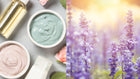 An assortment of gentle skincare products including two jars of creamy masks in soft colors, a bottle of facial oil, and a small container, paired with a blurred background of purple flowers, symbolizing soothing natural ingredients.